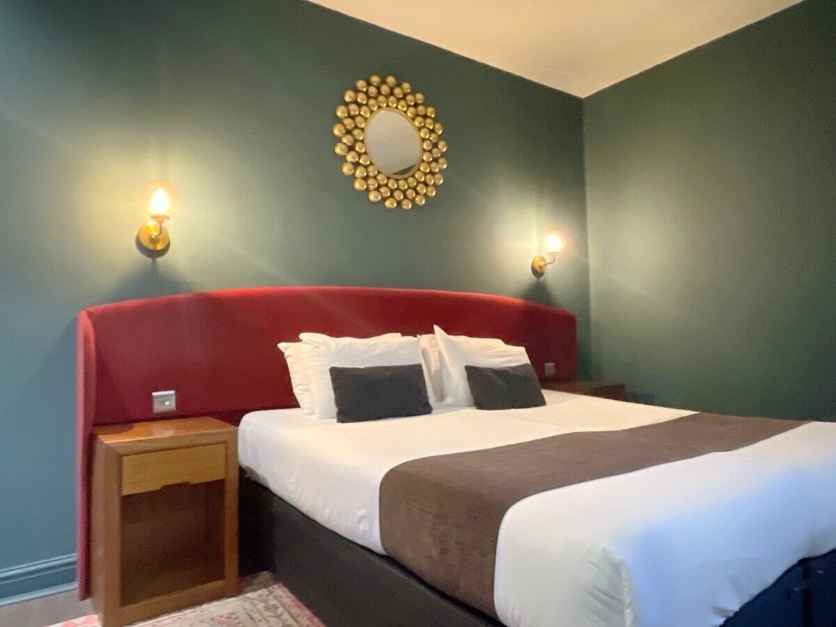 Un lit bien fait, avec une literie blanche et marron, deux tables de chevet avec des lampes et un miroir décoratif au mur.