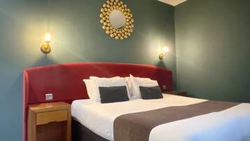 Un lit bien fait, avec une literie blanche et marron, deux tables de chevet avec des lampes et un miroir décoratif au mur.