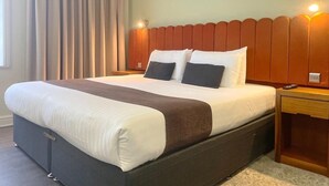Una cama bien hecha con cabecera marrón, una mesita de noche y una lámpara.