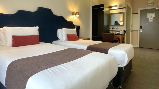 A hotel room with two beds, a desk, a chair, and a mirror. - HNFC Stays - Business En-Suit (Tyne and Wear)