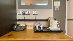 A hotel reception desk with a telephone, a tray with cups and a tray of pens, and a sign with a social media handle. - HNFC Stays - Business En-Suit (Tyne and Wear)