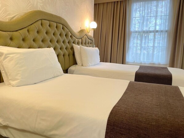 Two beds with white mattresses and matching pillows, upholstered headboards, and a throw blanket.