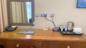 A hotel desk with a laptop, phone, and a tray with a kettle, cups, and a small box.