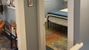 A room with a bed, a desk, and a chair. There is a door leading to another room.