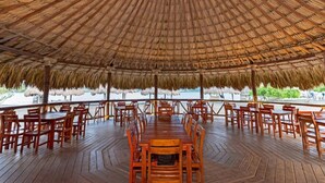 A covered dining area with wooden tables and chairs, a thatched roof, and a view of the sea. - Charming 2-bedroom house in Puerto Velero with WiFi, fitness room, AC (TUBARA)
