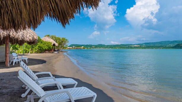 A beach with white lounge chairs and a thatched umbrella. - Charming 2-bedroom house in Puerto Velero with WiFi, fitness room, AC (TUBARA)