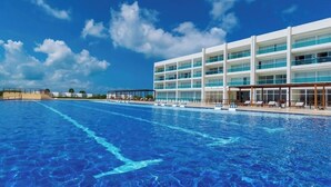 A hotel with a large swimming pool, multiple balconies, and a clear blue sky.