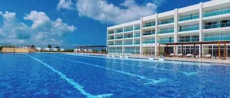 A hotel with a large swimming pool, multiple balconies, and a clear blue sky.