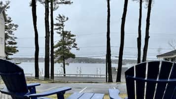 A patio with two Adirondack chairs and a small table, overlooking a body of water and a bridge.