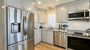 Una cocina moderna con electrodomésticos de acero inoxidable, armarios blancos y piso de madera.
