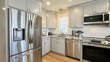 A modern kitchen with stainless steel appliances, white cabinetry, and a wooden floor.