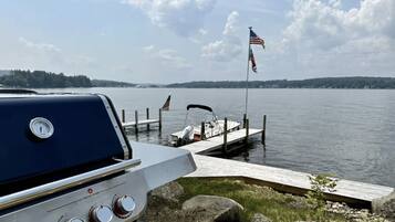 A boat docked at a pier with an American flag, a grill, and a calm lake in the background.