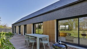 Uma casa moderna com um deck espaçoso, área de refeições com cadeiras e churrasqueira.