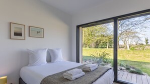 A bedroom with a large bed, two framed pictures on the wall, and a view of a garden through a large window. - L'Élégance | 115 m² | 4 + 2 guests | Design & Nature (Honfleur)