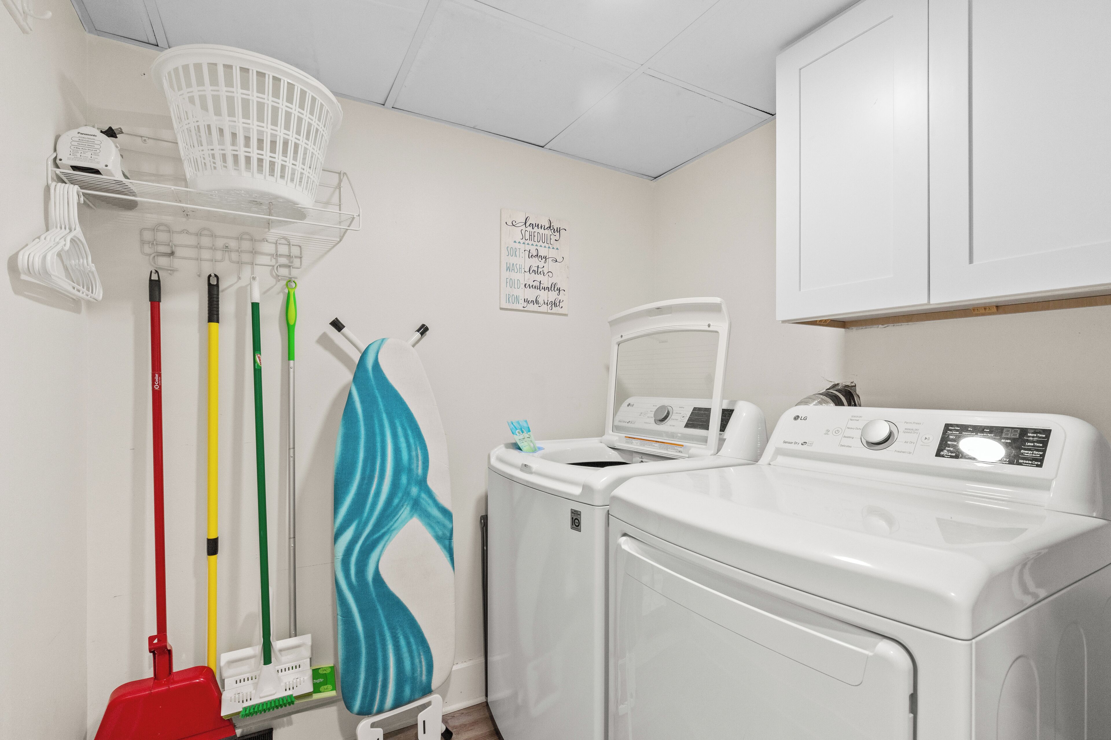 A laundry area with a washing machine, a drying rack, and a wall-mounted laundry schedule sign.