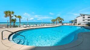 A swimming pool with lounge chairs and palm trees, surrounded by a fence and a building. - Watercrest Waves! Beachfront 2br/2ba Condo, Sleeps 8, Stunning Gulf Views! (Panama City Beach)