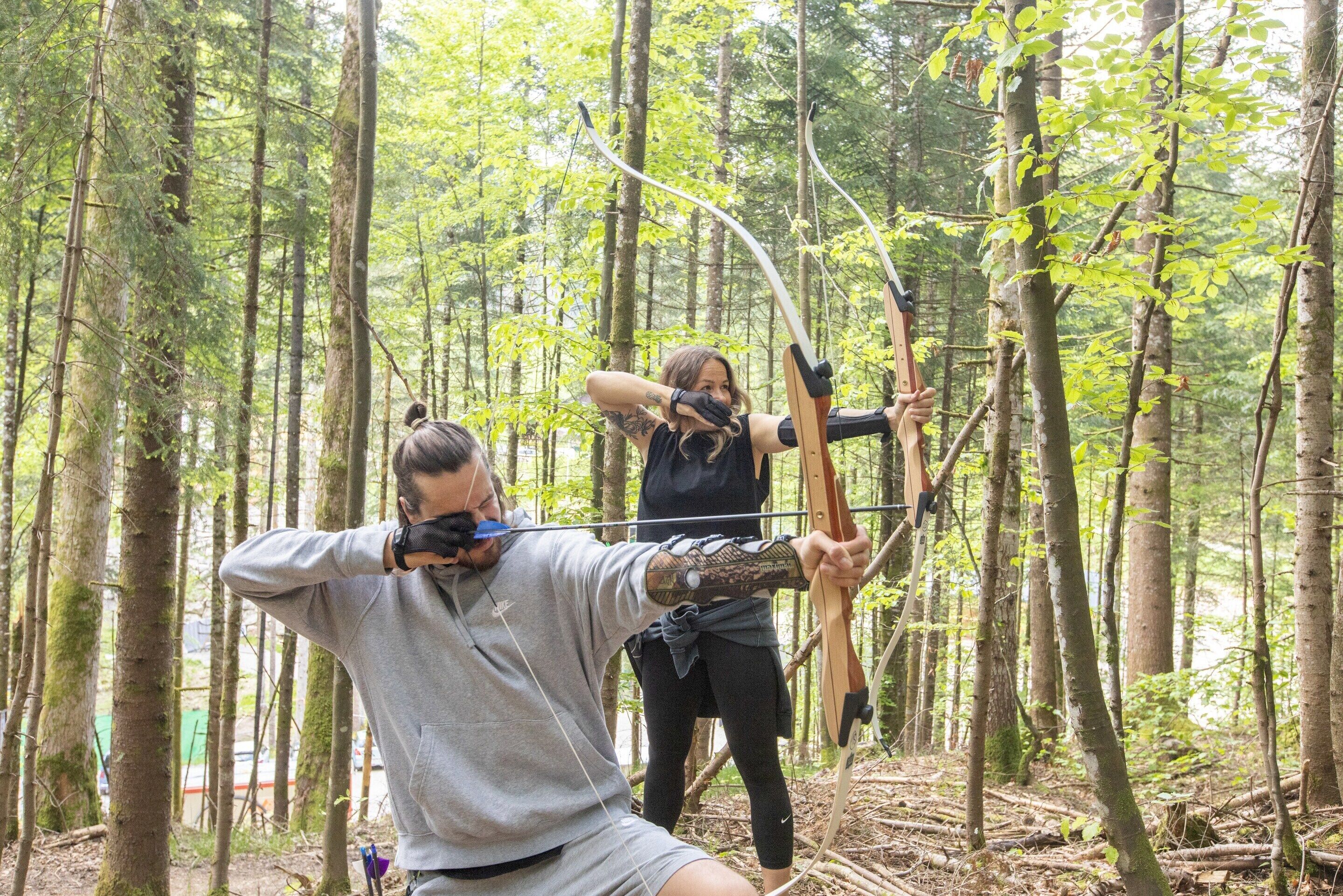 A person in a forested area aiming a bow.