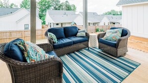 A covered outdoor seating area with wicker furniture and a striped rug.