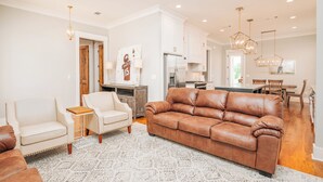 A spacious living room with a brown leather sofa, a white armchair, and a patterned rug.