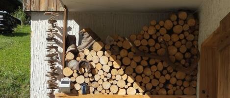 An outdoor patio with a barbecue grill, a wooden chair, and a stack of firewood.