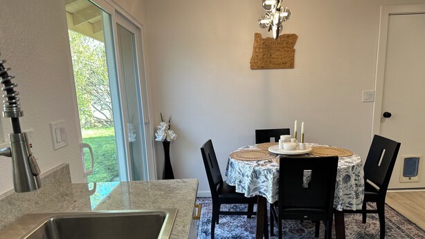 A modern kitchen with a stainless steel sink, a dining area with a round table and chairs, and a decorative wall piece. - Eugene Escape Close to Airport & Peaceful (Eugene)