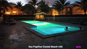 A swimming pool at night with a view of palm trees and a building in the background.