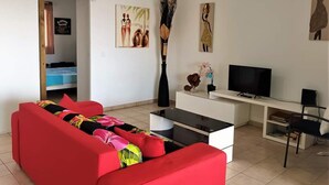 A living room with a red sofa, a TV, a white desk, and artwork on the walls.