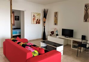 A living room with a red sofa, a TV, a white desk, and artwork on the walls. - T2*** at Crystal Beach on the edge of the Saint-François lagoon. Swimming pools and beach! (Saint-François)