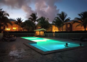 A swimming pool at night with a view of palm trees and a building in the background. - T2*** at Crystal Beach on the edge of the Saint-François lagoon. Swimming pools and beach! (Saint-François)