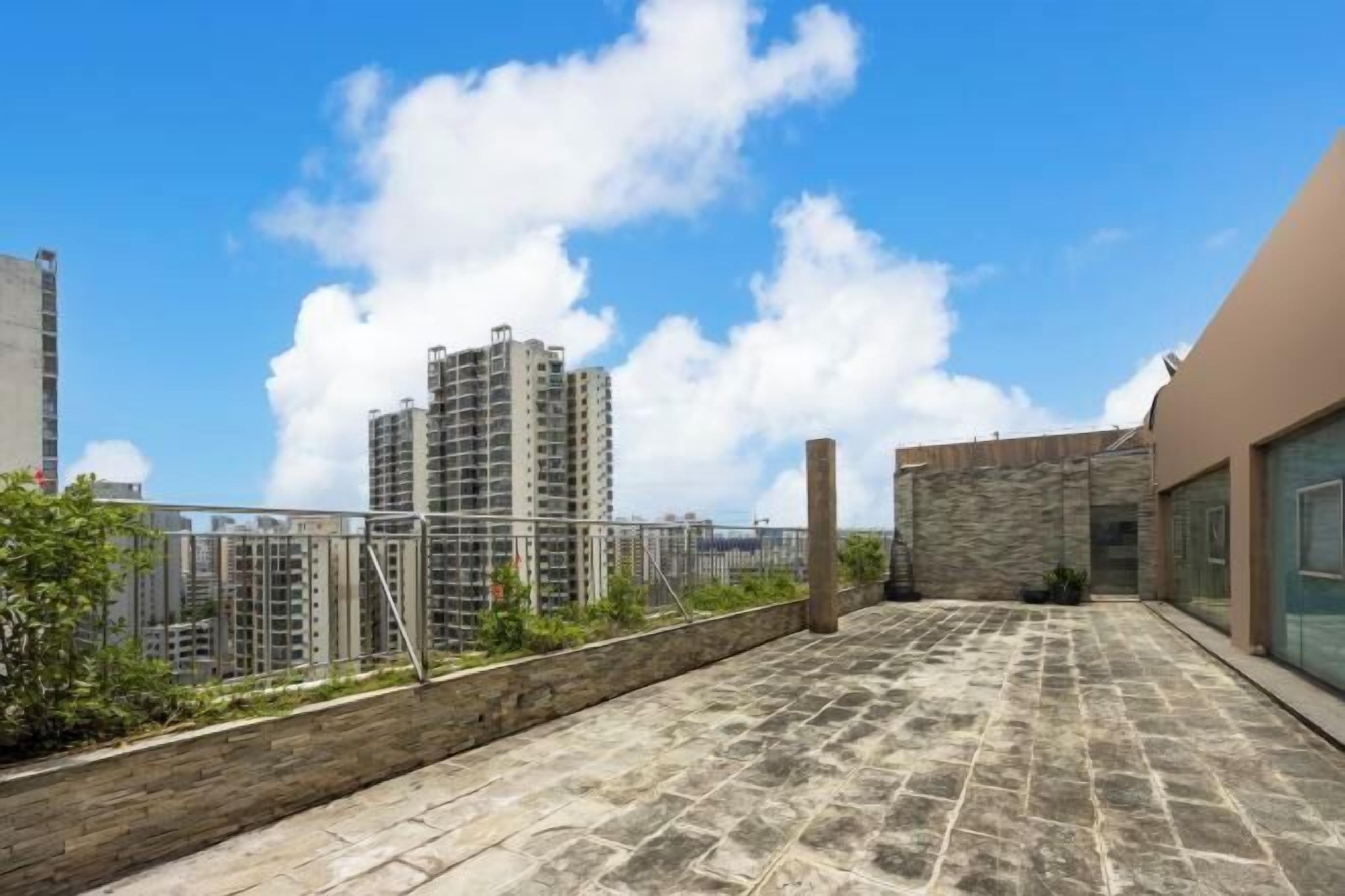 A rooftop terrace with a stone floor, a stone wall, and a view of high-rise buildings.
