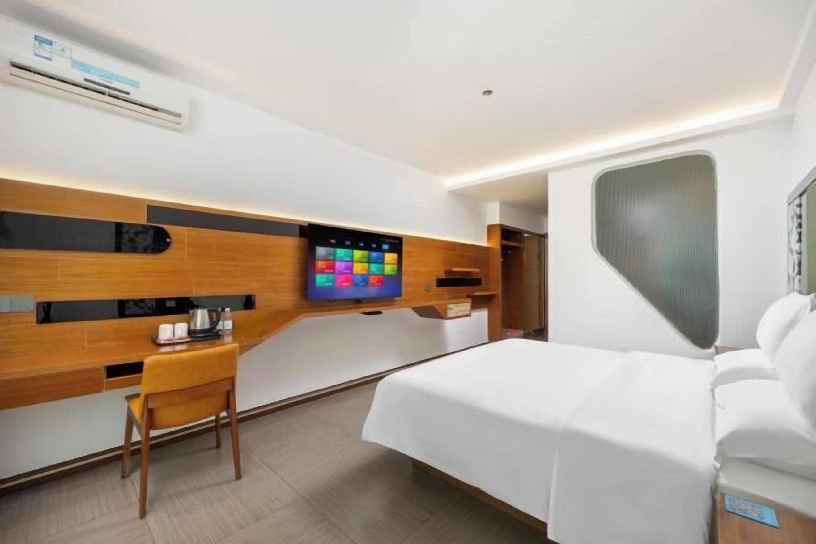 Ein modernes Hotelzimmer mit Bett, Schreibtisch, Stuhl, Fernseher und Klimaanlage.