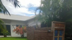 A house with a fenced yard, a potted plant, and a door with a decorative design. - Cosy studio in large garden with trees, terrace with jacuzzi (Saint-Louis)