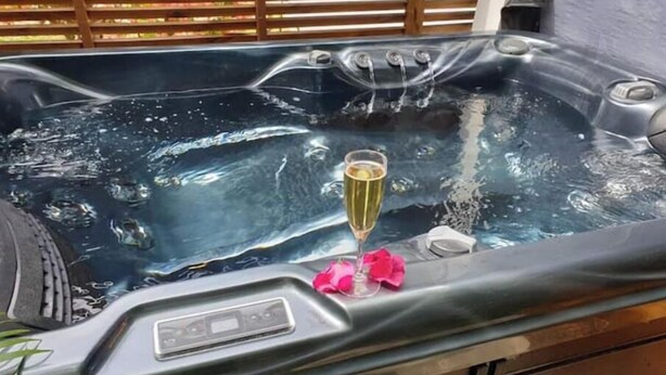 A hot tub with a control panel, a glass of champagne, and pink flower petals. - Cosy studio in large garden with trees, terrace with jacuzzi (Saint-Louis)