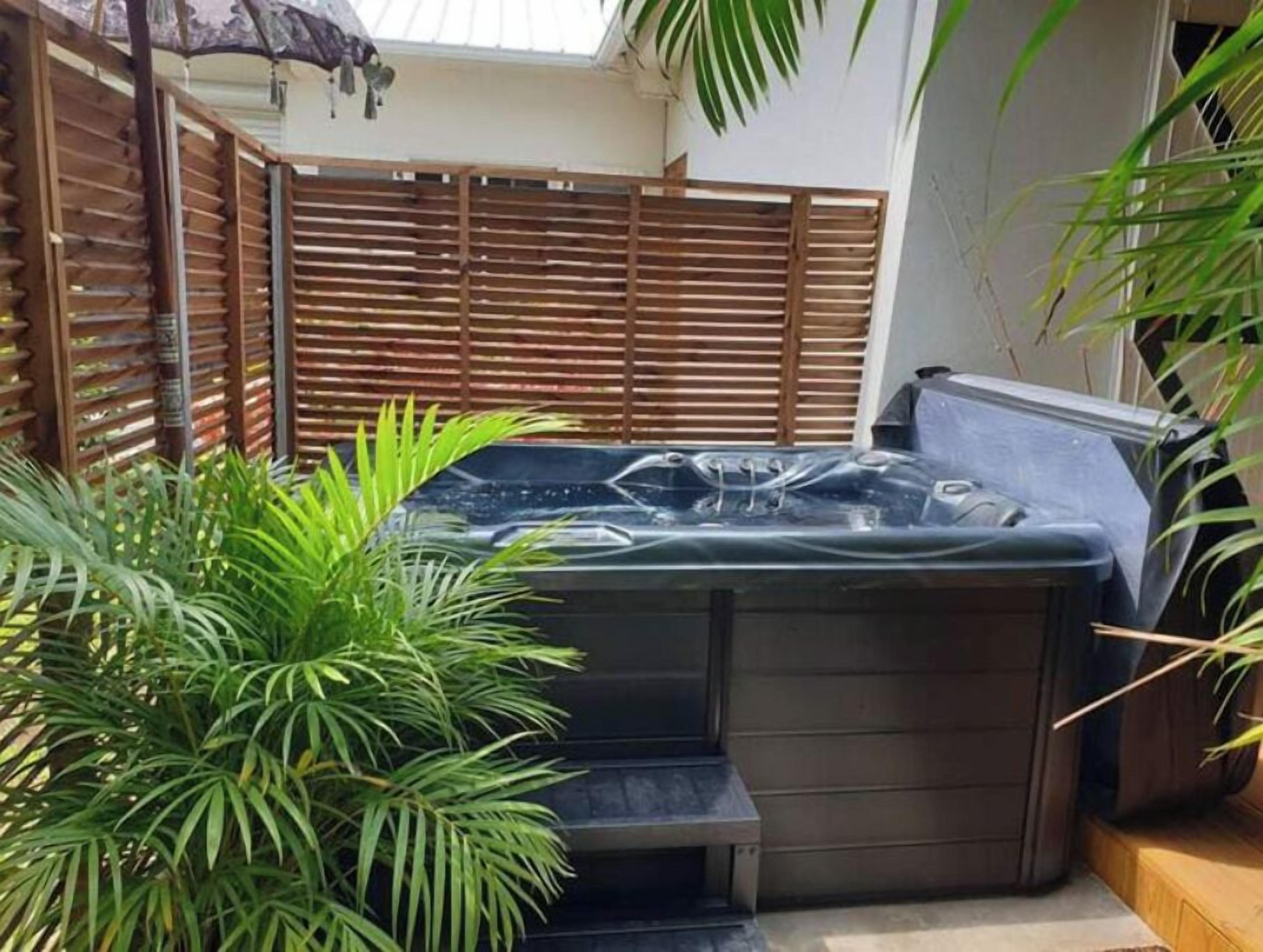 A hot tub in a covered outdoor area with a wooden fence and potted plants.