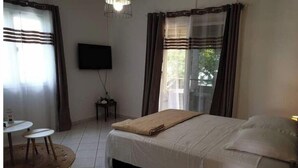 A hotel room with a bed, a TV, a small table, and a lamp. - Cosy studio in large garden with trees, terrace with jacuzzi (Saint-Louis)