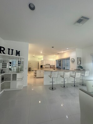 A modern kitchen with white cabinetry, a central island with bar stools, and a large window. - 3-bedroom in Davie . WiFi, AC. Pool ,near to Sawgrass Mall, Hard Rock ,F Garden, (Davie)