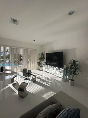 A modern living room with a flat-screen TV, a glass coffee table, and a sofa. - 3-bedroom in Davie . WiFi, AC. Pool ,near to Sawgrass Mall, Hard Rock ,F Garden, (Davie)