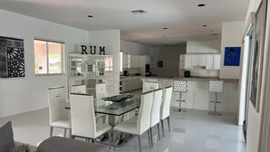 A modern kitchen with white cabinets, a central island, and a dining area with a glass table and white chairs.