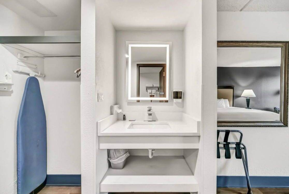A modern bathroom with a white sink, a mirror, and a blue ironing board.