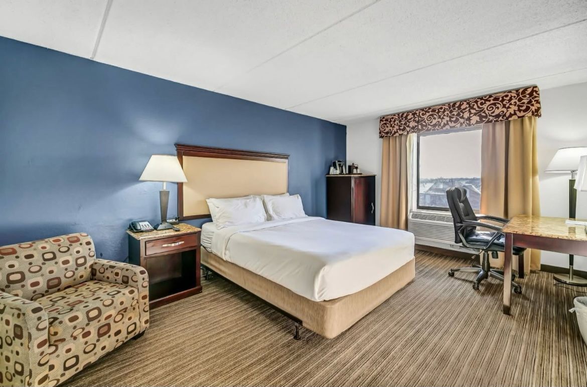 Une chambre d’hôtel avec un lit, un bureau, une chaise, un canapé et une vue sur la ville.