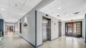 A clean, modern hallway with an elevator, exit sign, and a door with a glass panel.