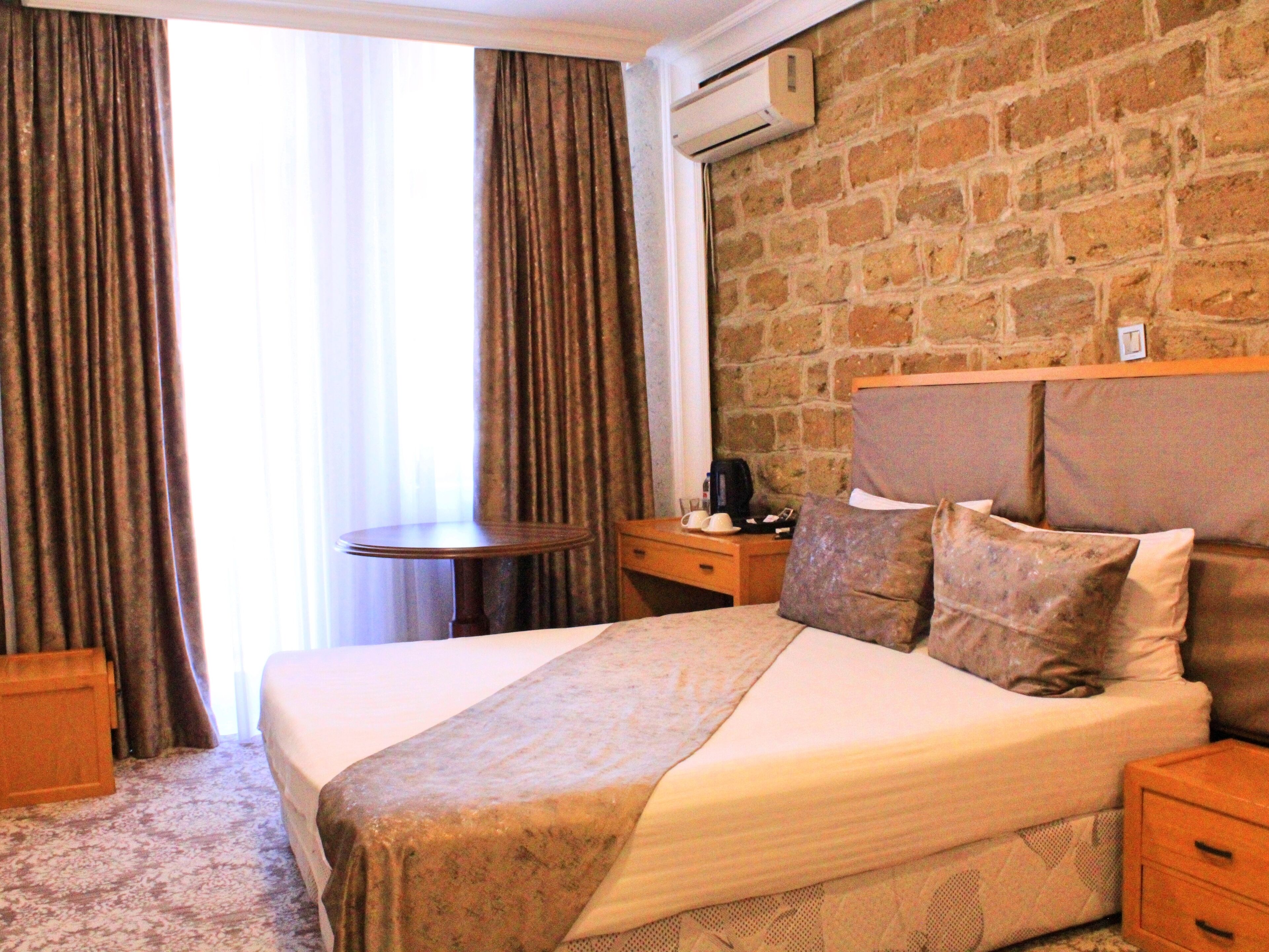A hotel room with a large bed, a wooden headboard, a small round table, a nightstand, and a brick wall.