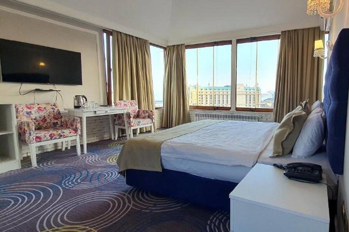 A hotel room with a bed, a desk, a chair, a TV, and a view of the city.