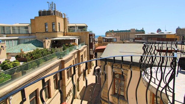 Una terraza en la azotea con barandilla de cristal, vista panorámica de la ciudad y cielo despejado.