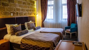 Habitación de hotel con dos camas, una pared de piedra, aire acondicionado, televisor, una silla y una mesa con mandos a distancia.