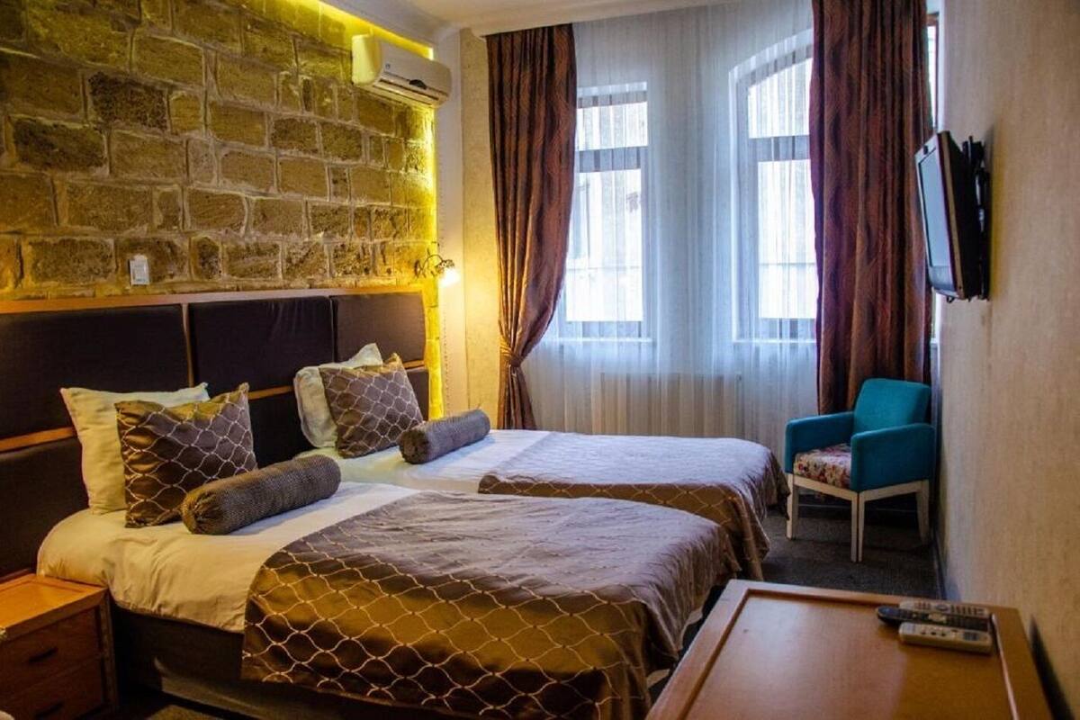 A hotel room with two beds, a stone wall, an air conditioning unit, a TV, and a chair.