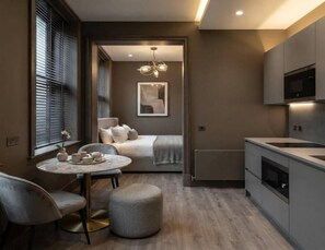 Une cuisine compacte dotée d’appareils électroménagers modernes, un coin repas avec une table ronde et des chaises, et un coin salon confortable avec un canapé et des coussins.