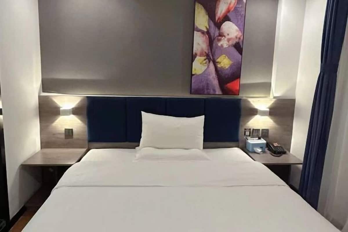 A hotel room with a large bed, two bedside tables, a headboard, and a wall-mounted artwork.