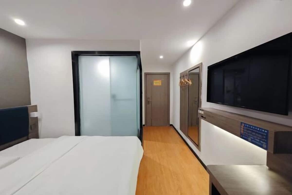 A hotel room with a bed, a television, a mirror, and a wooden floor.
