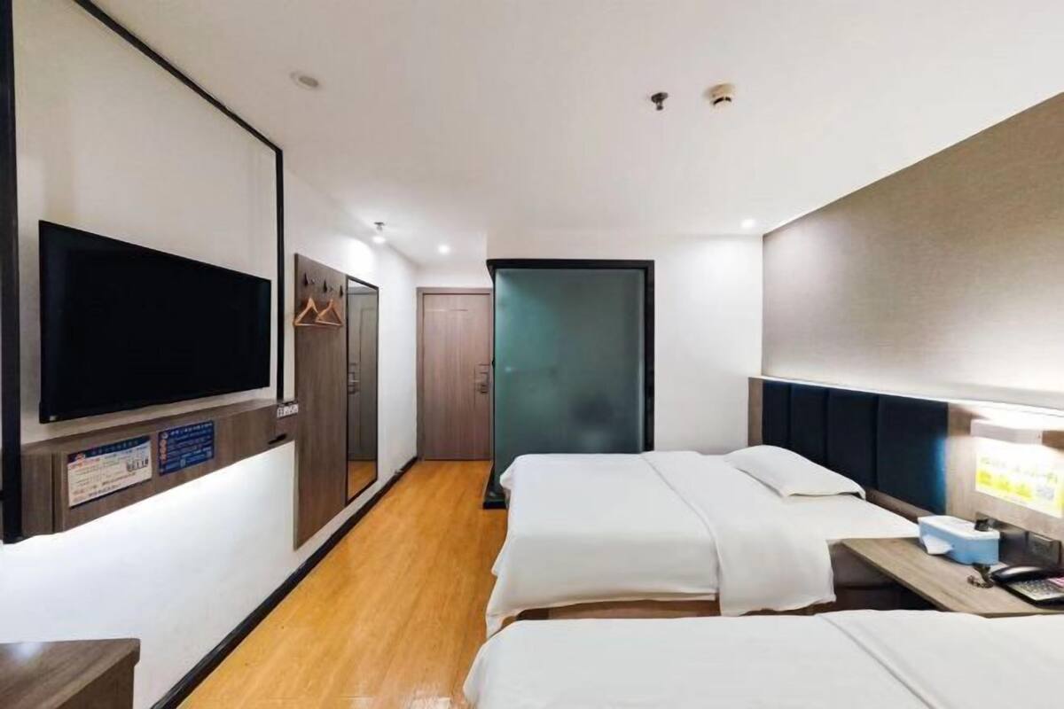 A hotel room with two beds, a TV, a desk with a computer, and a door leading to a bathroom.